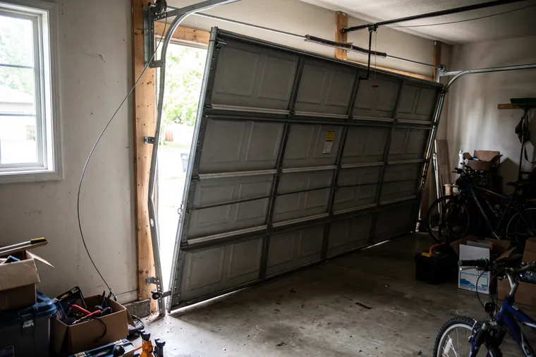 A sectional garage door hanging crooked in the opening after the rollers on one side came out of the track
